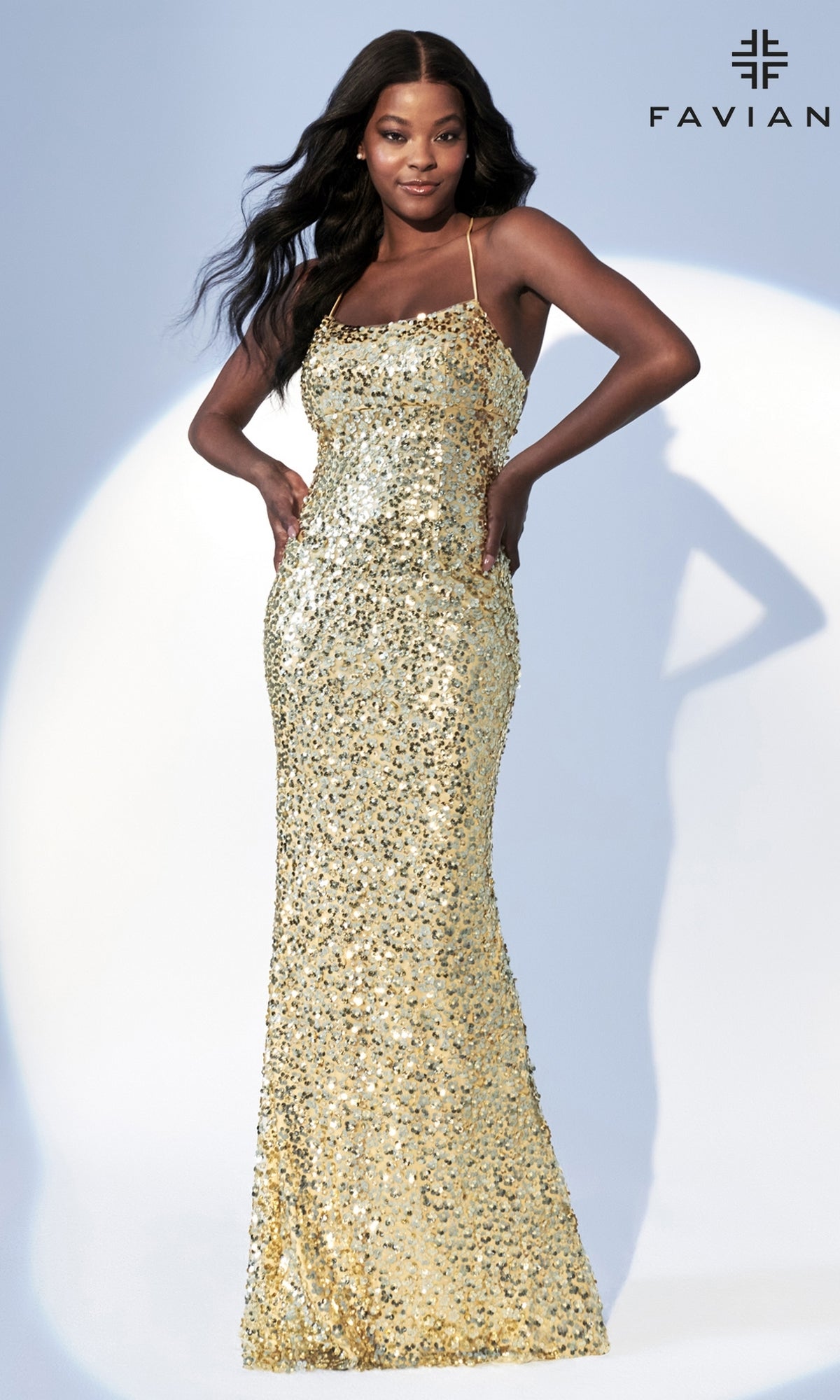 A woman wears the Faviana Empire-Waist Long Sequin Prom Dress 11033, a fitted, floor-length gold gown with thin straps, standing against a light background with the Faviana logo in the corner.